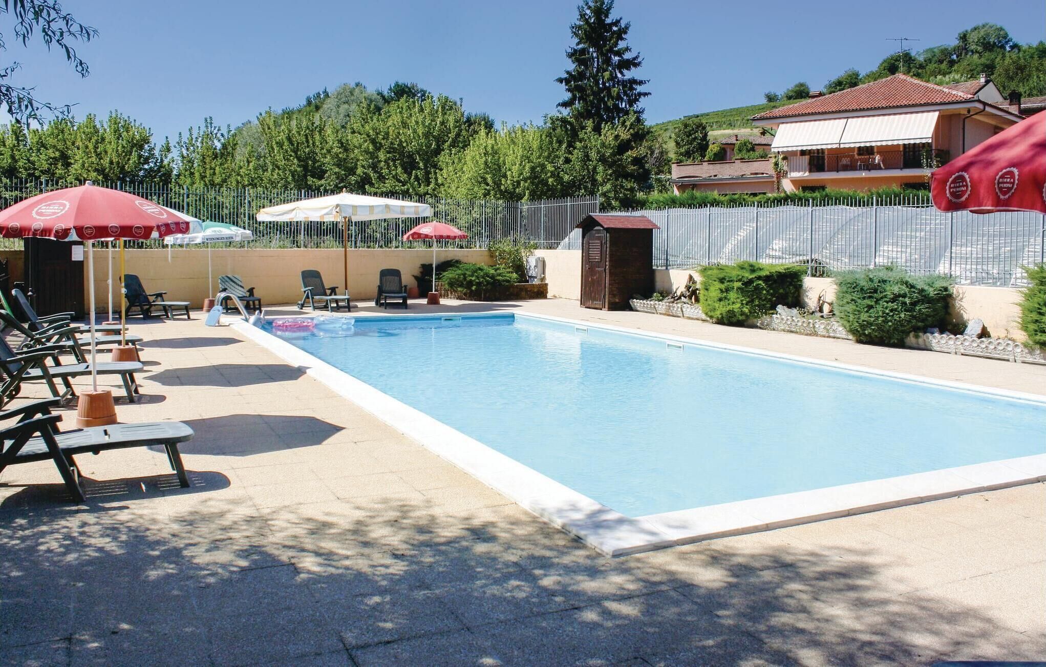 A swimming pool with lounge chairs and umbrellas, surrounded by a fence and greenery.