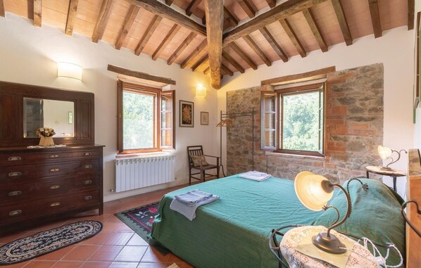 A bedroom with a wooden ceiling, a bed with a green bedspread, a dresser with a mirror, and two windows with wooden frames.