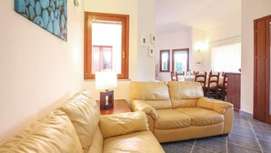 Una sala de estar con un sofá de cuero color beige, una puerta de madera y un comedor con mesa y sillas.