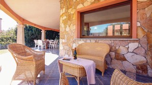 Un patio al aire libre con muebles de mimbre, una pared de piedra y un ventanal grande.