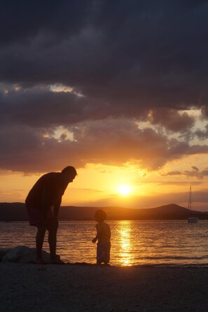 Enjoy a serene beachside moment with a parent and child, surrounded by rolling hills and a sailboat on the horizon.