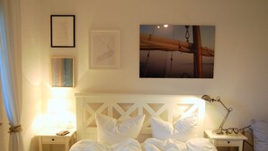 Un lit bien fait, avec du linge de lit blanc, une lampe de chevet et un tableau encadré au mur.