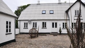 A white building with a tiled roof, a stone-paved courtyard, and a small tree.
