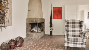 A room with a stone fireplace, a plaid armchair, and decorative items on the floor.