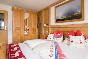 Ein Schlafzimmer mit Bett, einem Holzschrank, einem Nachttisch, einer Lampe und einem gerahmten Landschaftsbild mit Regenbogen.