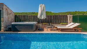 En swimmingpool med solstolar och ett bubbelbad, omgiven av ett trästaket och en stenmur.