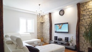 Ett modernt vardagsrum med en vit soffa, ett soffbord i glas, en tv som är monterad på en vägg av sten och en väggpanel i trä som ger rummet en accentfärg.