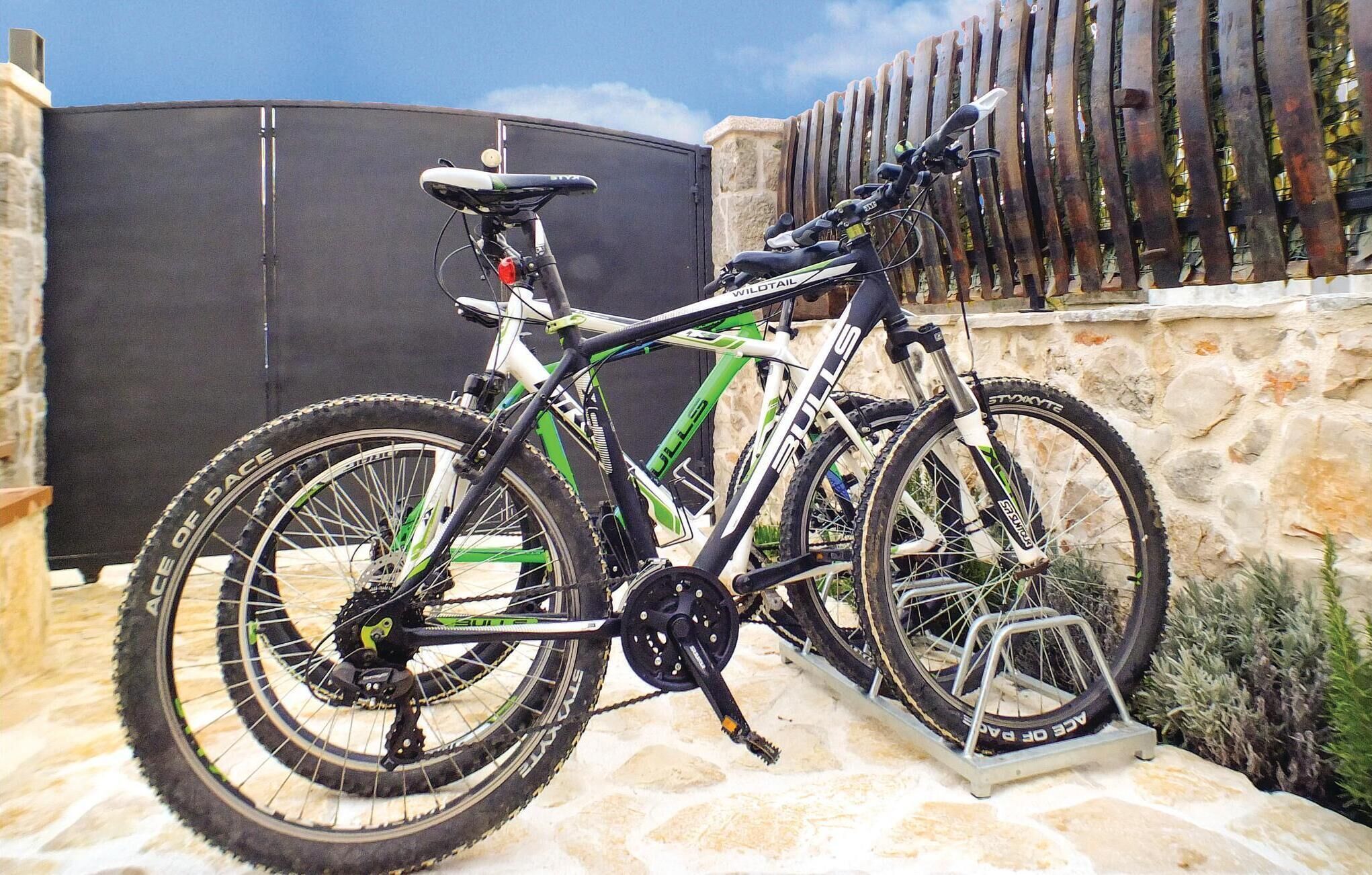 Uma bicicleta de montanha estacionada em um pátio de pedra, com um muro de pedra e uma cerca de madeira ao fundo.