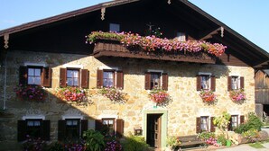 A stone building with multiple windows, some with shutters, and flower boxes on the exterior. - Double room 4 - Moadl farm (Miglberg)