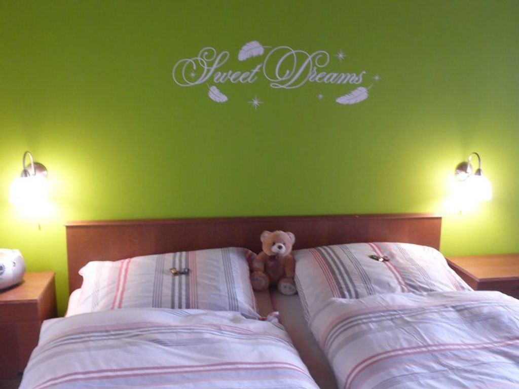 A room with two beds, a teddy bear on the left bed, and a wall with 'Sweet Dreams' written on it.