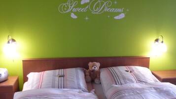 A room with two beds, a teddy bear on the left bed, and a wall with 'Sweet Dreams' written on it.