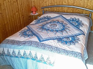 Una cama con una colcha y almohadas de diseño azul y blanco, una pared de madera y una mesita de noche con una lámpara.