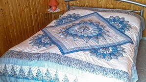 Een bed met een blauw-wit gebed en kussens, een houten wand en een klein tafeltje met een lamp.