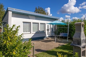 A modern building with a flat roof, a patio area with a table and umbrella, and a stone structure. - Bungalow on the edge of the forest - Bungalow (Barth)