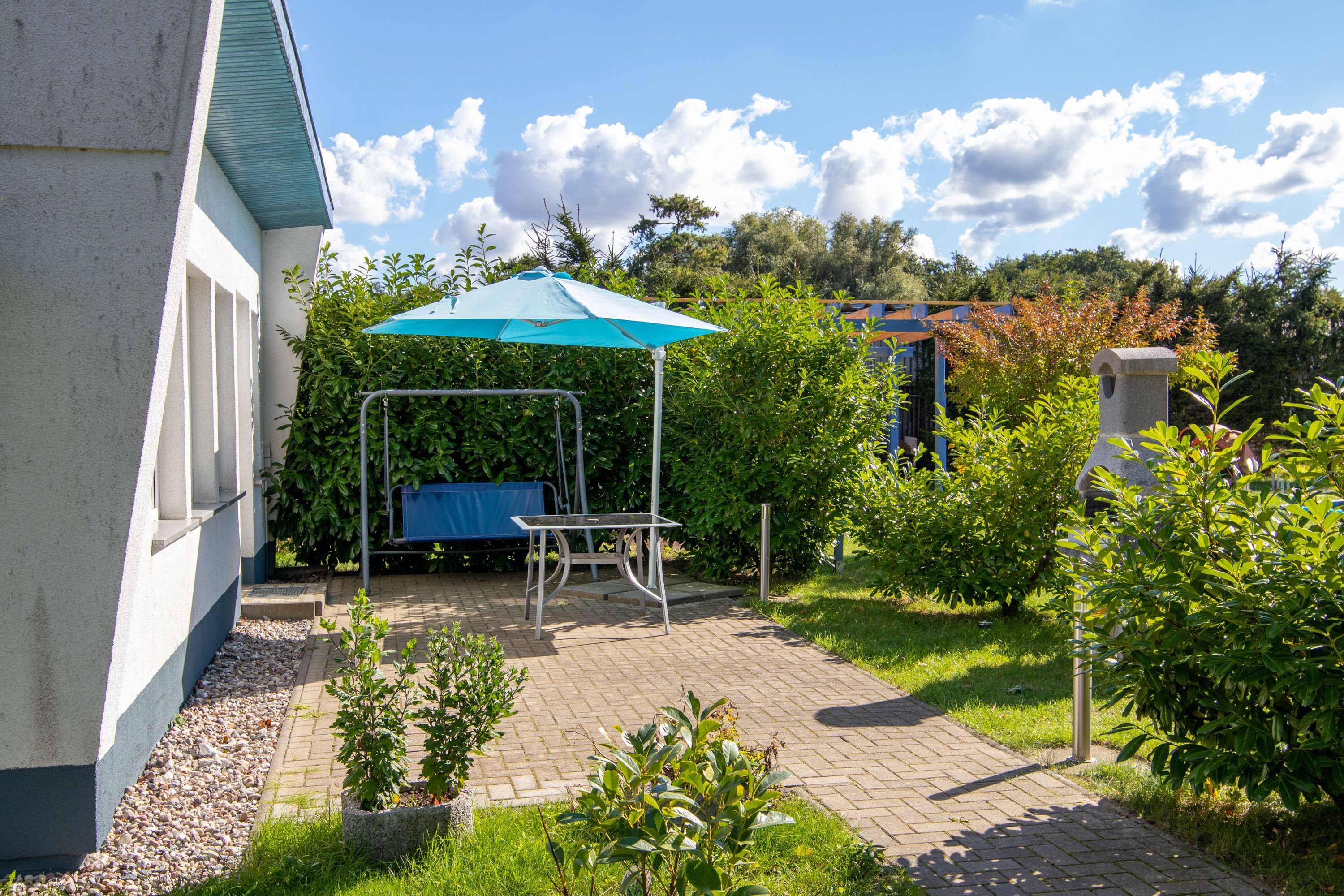 Eine Terrassenfläche mit Tisch und Stühlen, ein überdachter Sitzbereich und ein Garten mit verschiedenen Pflanzen.