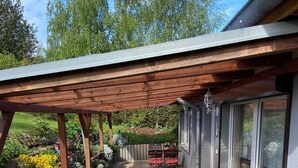 A covered patio with a wooden pergola, outdoor seating, and a garden with various plants and flowers.