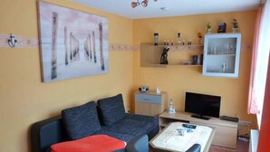A living room with a sofa, coffee table, TV, and shelves with decorative items.