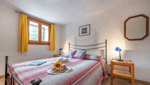 A bedroom with a bed, a bedside table, a lamp, a window with curtains, a framed picture on the wall, and a mirror. - Holiday apartment mit Terrasse (Pittulongu)