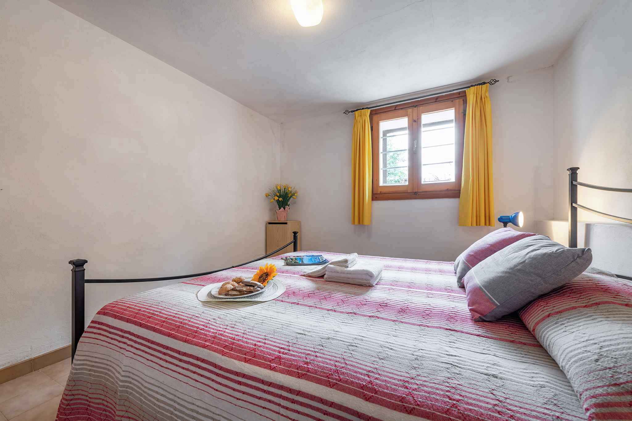 Un lit simple avec une couvre-lit à rayures, une table de chevet avec une lampe et une fenêtre avec des rideaux jaunes.
