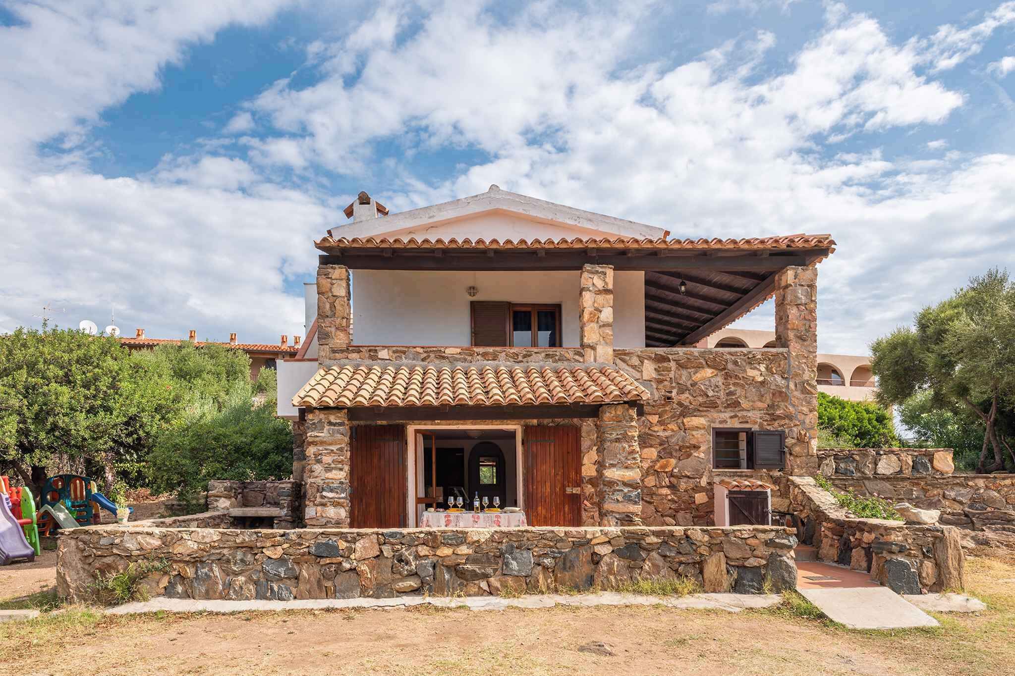 A two-story stone house with a tiled roof, a stone staircase, and a small patio area.
