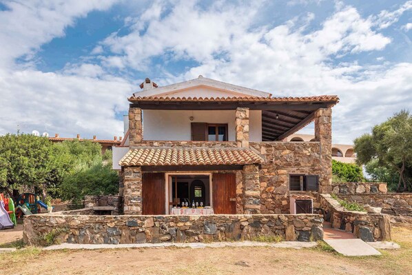 A two-story stone house with a tiled roof, a stone staircase, and a small patio area.