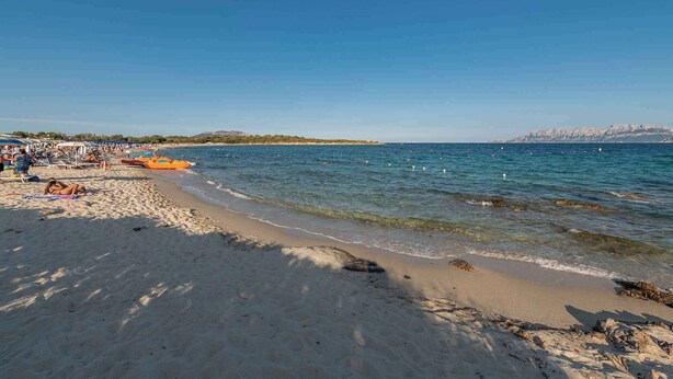A beach with clear blue water, sandy shore, and a rocky outcrop. - Holiday apartment mit Terrasse (Pittulongu)
