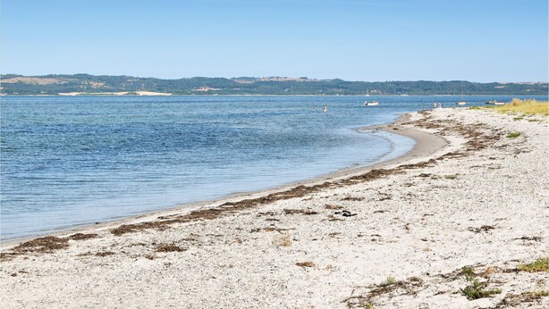 Una spiaggia con acqua cristallina, una costa sabbiosa e colline in lontananza.