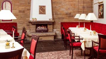 A restaurant with red upholstered seating, a stone fireplace, and white tablecloths.