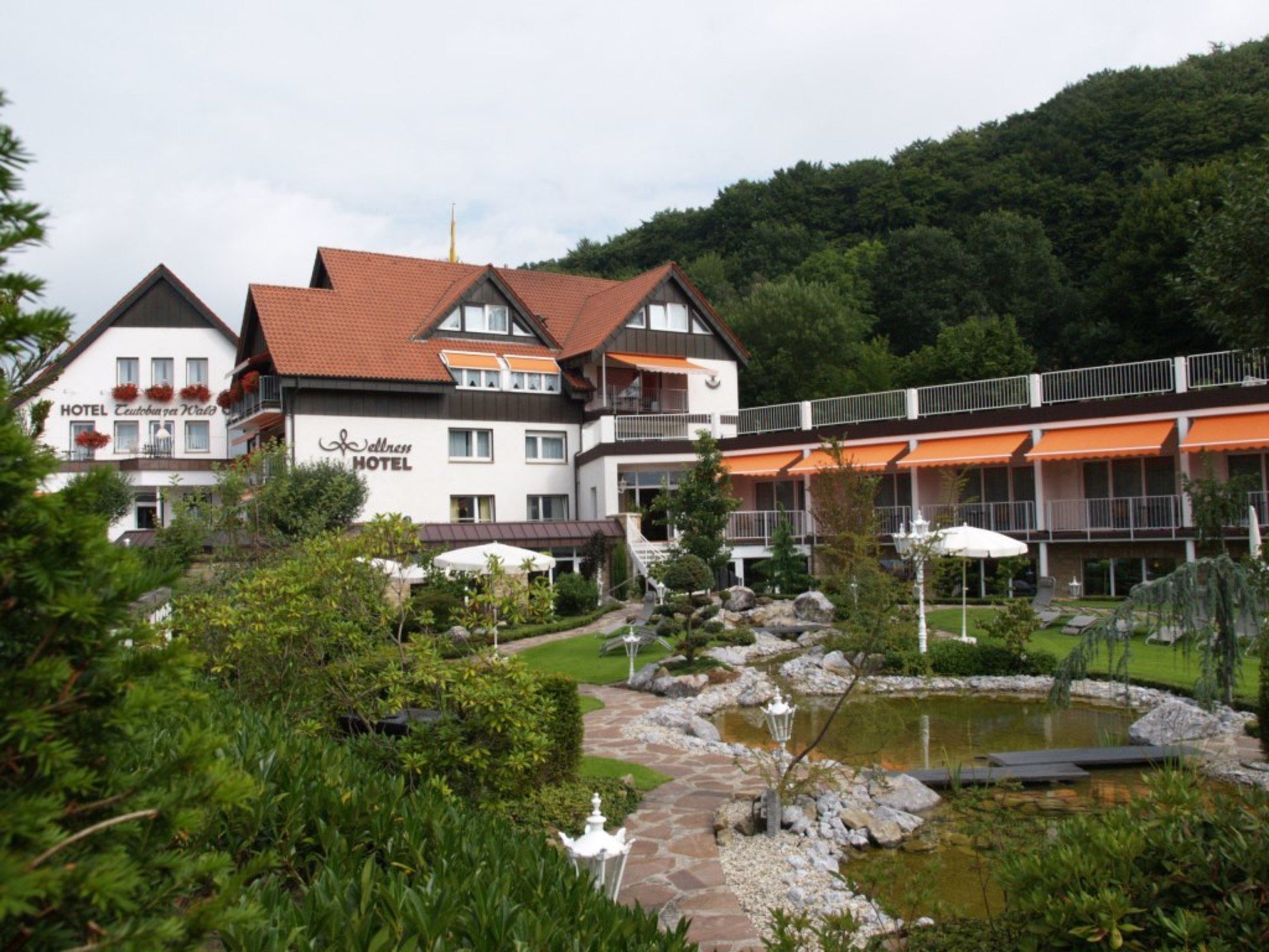 Un hotel con jardín, estanque y montañas al fondo.