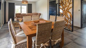 Un coin repas avec une table en bois et des chaises en osier, un canapé et un élément décoratif en bois fixé au mur.