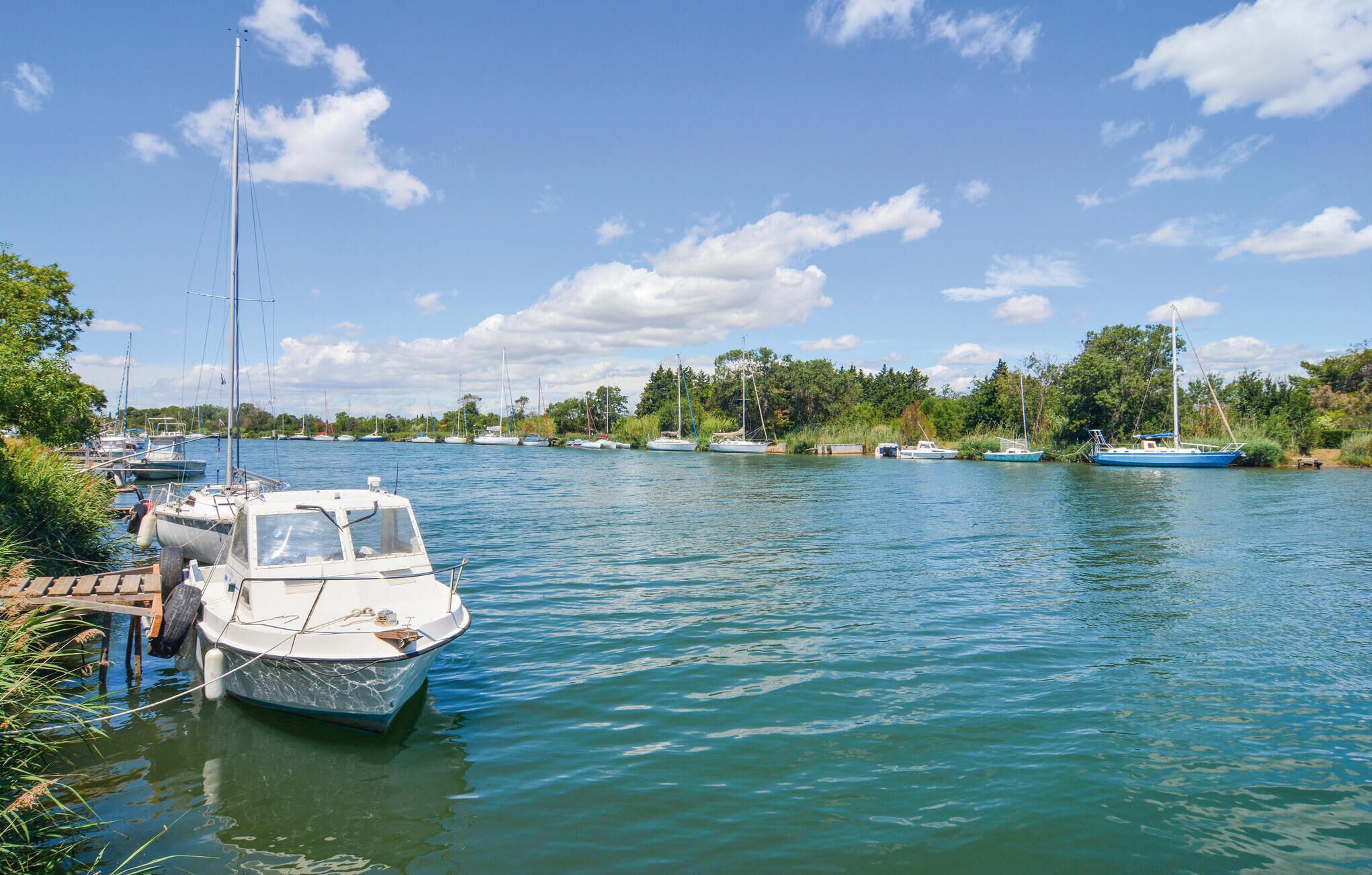 Ein ruhiger Fluss mit an den Ufern vertäuten Booten, umgeben von Grün und Bäumen.