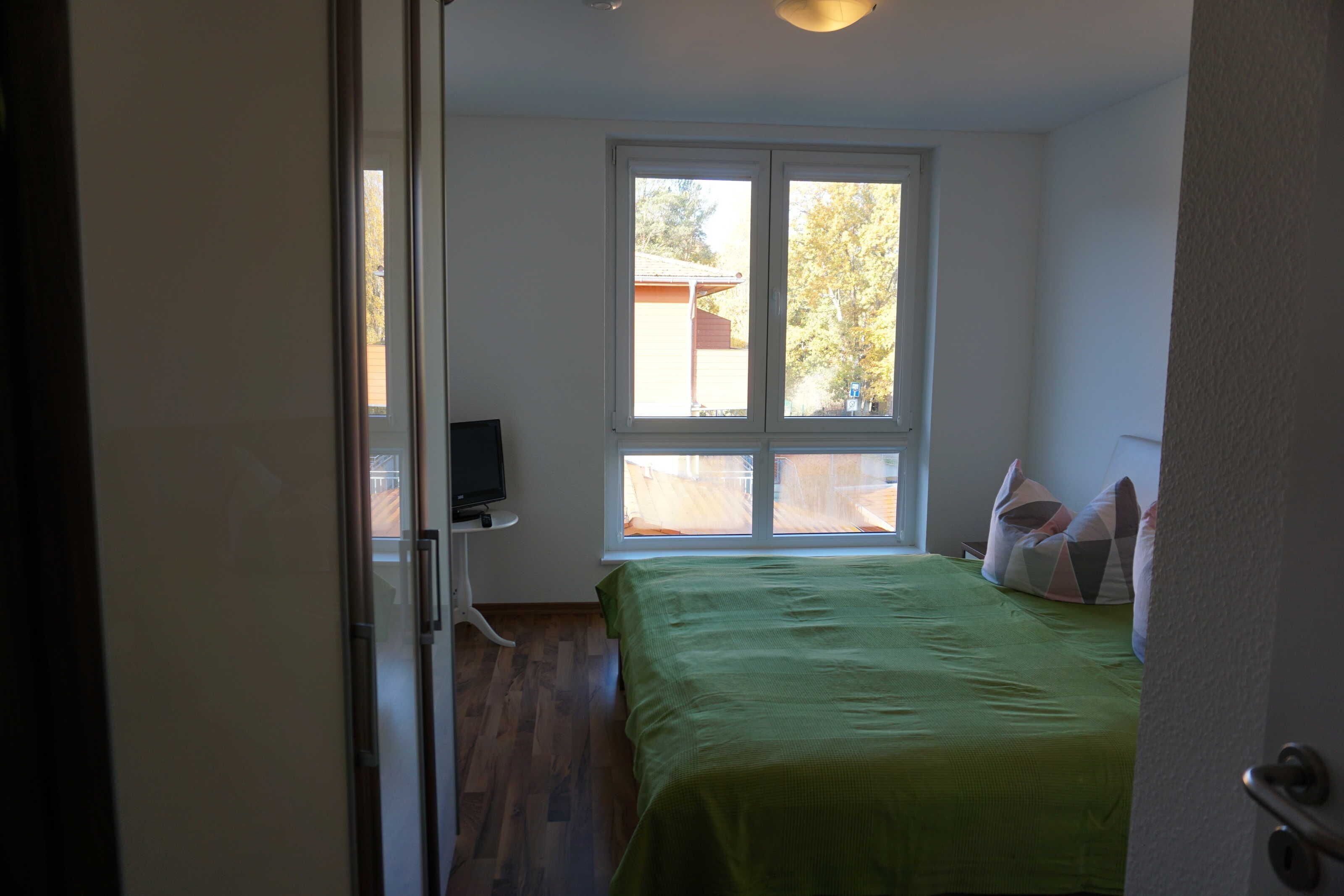 A bedroom with a bed, a window, and a television on a stand.