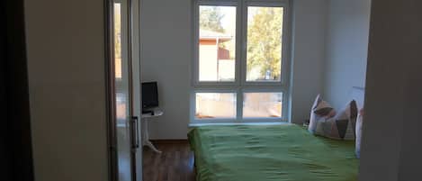 Un dormitorio con cama, ventana y televisor sobre un mueble.