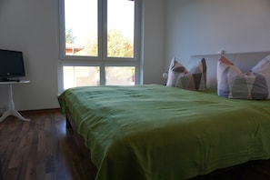 Una habitación con cama, televisión sobre un mueble y ventana.