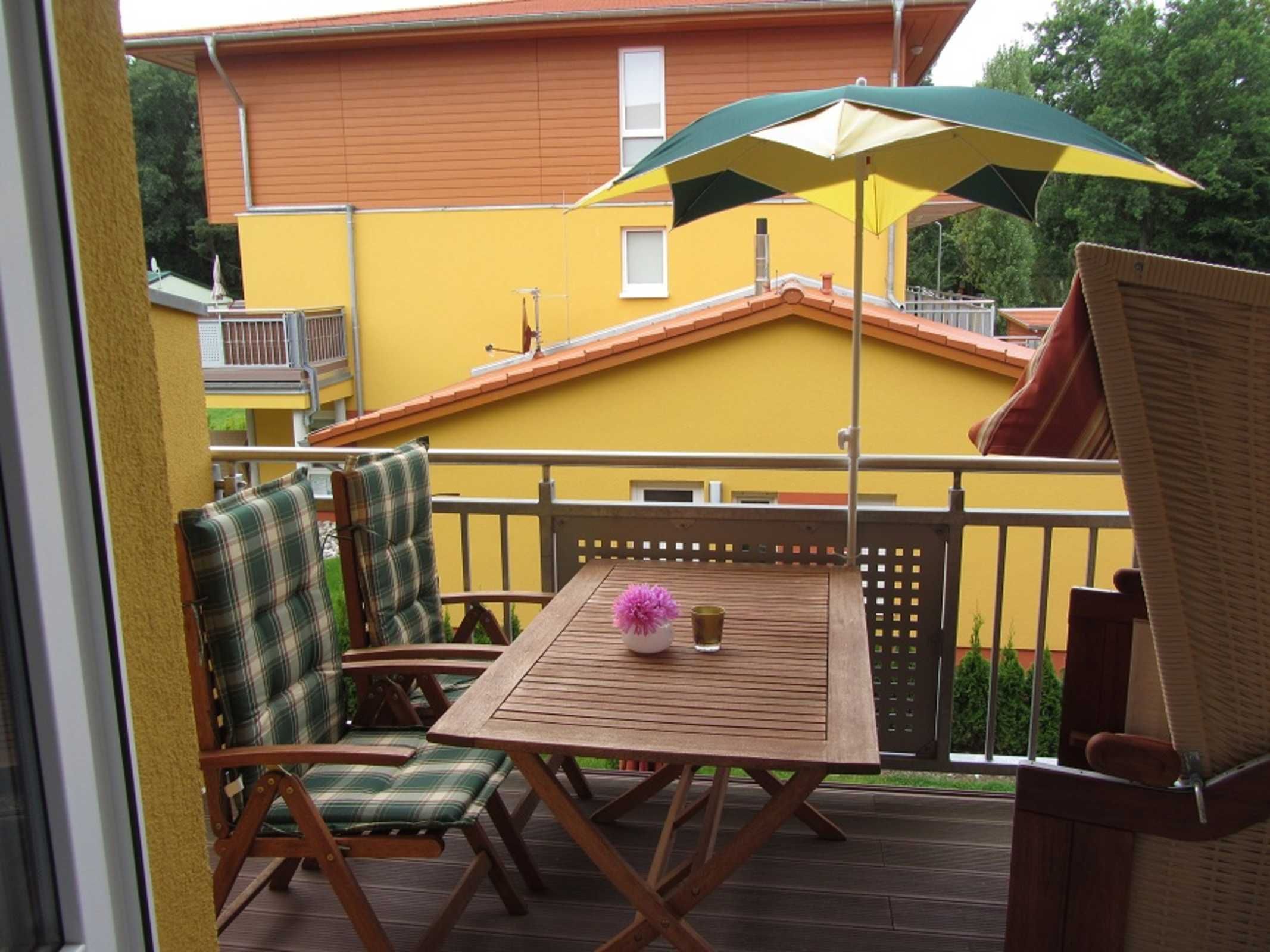 A wooden deck with a table and chairs, an umbrella, and a building in the background.