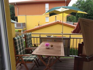 En träveranda med ett bord och stolar, ett parasoll och en byggnad i bakgrunden.