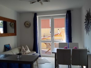 Una habitación con una mesa de comedor, sillas, un sofá, un reloj y vistas a un balcón exterior a través de un ventanal.