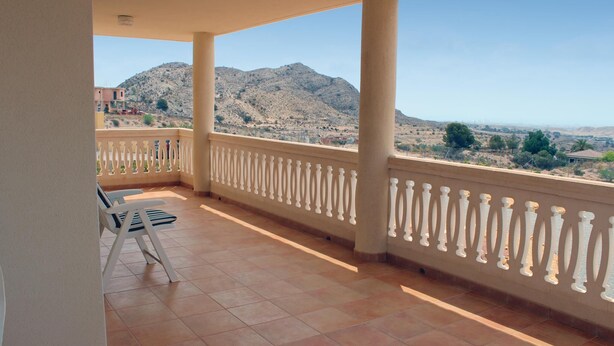 Ein Balkon mit gefliestem Boden, weißem Geländer und Blick auf eine Berglandschaft.