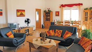 Ein Wohnzimmer mit einer Sofagarnitur, einem Couchtisch, einem Fernseher und einem Ventilator.