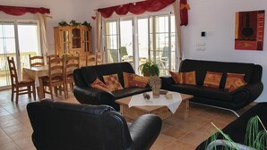 Ein Wohnzimmer mit zwei schwarzen Sofas, einem Couchtisch und einem Essbereich mit Holzmöbeln.