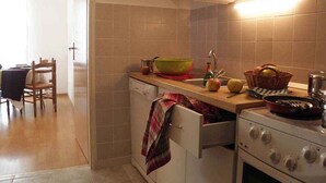A kitchen with a stove, sink, and cabinets. There is a chair and a table in the adjacent dining area.