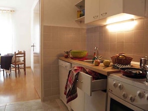 Cozinha com fogão, pia e armários. Há uma cadeira e uma mesa na área de refeições próxima.