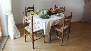 A dining area with a table set for four, wooden chairs, a white tablecloth, and a painting on the wall.