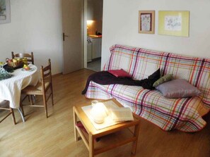 Un salón acogedor con un sofá de cuadros, una mesa de centro de madera y un comedor con sillas y una mesa dispuesta para dos.