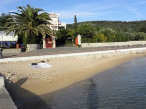 Una playa con un muro de piedra, una palmera y un edificio al fondo.