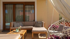 Ein sonniger Außenbereich mit Sitzgelegenheiten, einer Couch, einem Holztisch und einem Hängesessel.