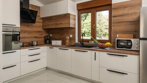 Eine moderne Küche mit weißen Schränken, einem eingebauten Backofen, einer Kaffeemaschine und einem Fenster mit Blick auf Grünflächen.