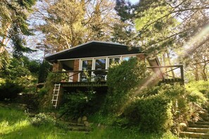 A rustic cabin with a stone foundation, wooden deck, and a ladder leading to a wooden staircase. - House Incognito, Germany (Sellin)