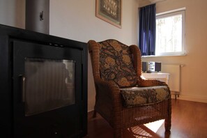 Een kamer met een open haard, een rieten fauteuil, een radiator en een raam met gordijnen.