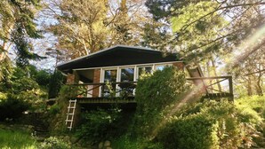 A rustic cabin with a stone foundation, wooden deck, and a ladder leading to a wooden staircase.